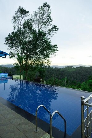 Une piscine à débordement offrant une vue sur un arbre et un paysage lointain.