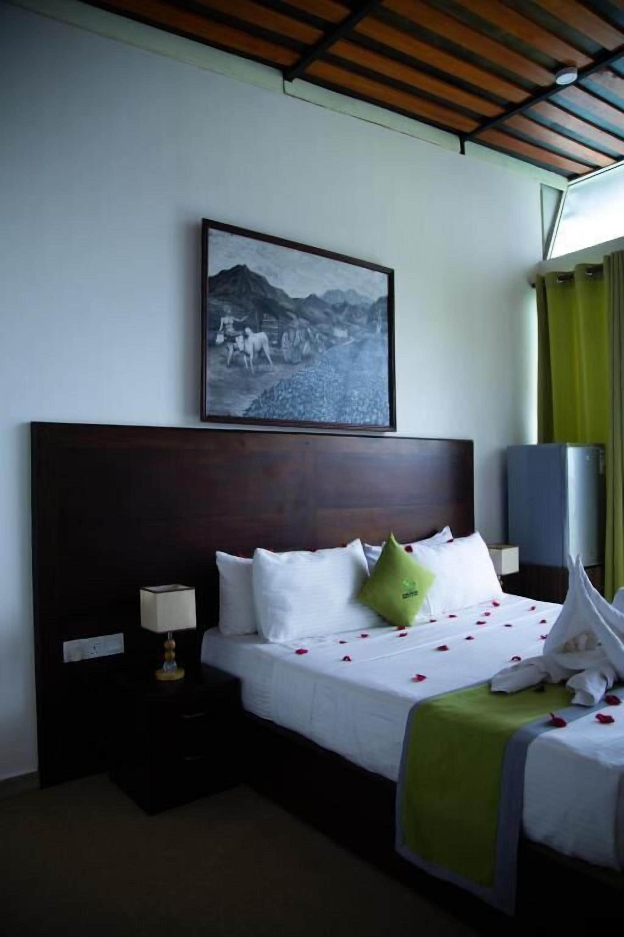 A hotel room with a bed, a nightstand, a lamp, a picture on the wall, and a window with curtains.