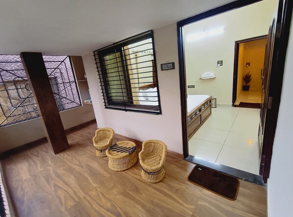 A room with a bed, a window with bars, wicker chairs, and a tiled floor. - Mango Tree 3BHK Apartment (Ujjain)