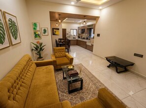 A living room with a sofa set, a coffee table, and a dining area with chairs and a table. - Mango Tree 3BHK Apartment (Ujjain)
