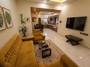 A living room with a sofa set, a coffee table, and a TV. - Mango Tree 3BHK Apartment (Ujjain)