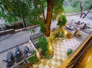 A rooftop terrace with a checkered floor, potted plants, and two parked motorcycles. - Mango Tree 3BHK Apartment (Ujjain)