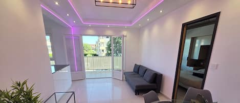 A modern living room with a sofa, chairs, a glass coffee table, and a potted plant.
