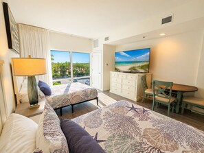 Ein Hotelzimmer mit Bett, Schreibtisch, Fernseher und Blick auf den Strand.