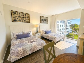 A hotel room with two beds, a nightstand, a lamp, a chair, and a view of the city. - 4th-Floor Studio | Walk to Beach | Pool, Beach Tram | Luau II 6421, Sandestin (Miramar Beach)