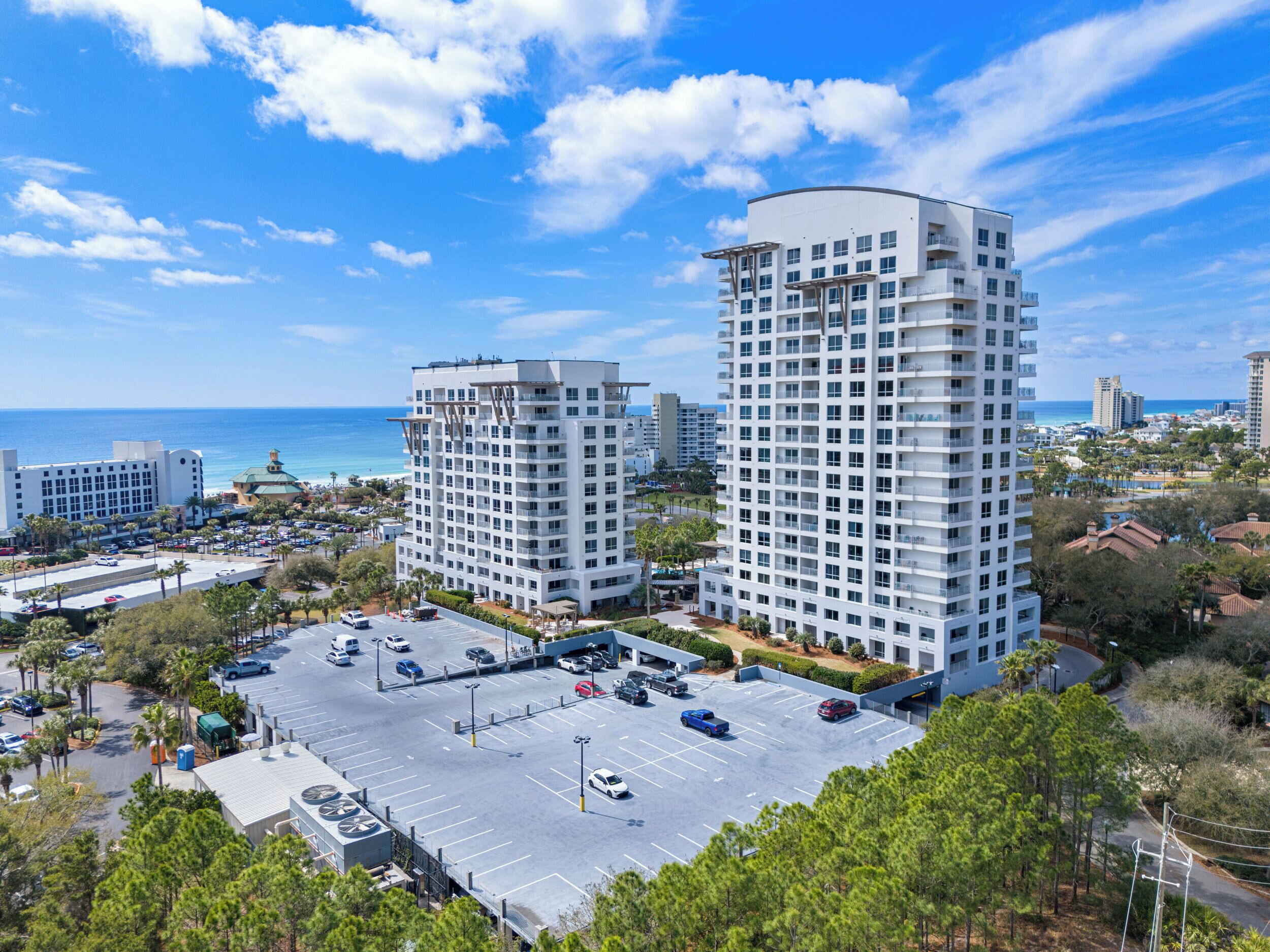 A high-rise hotel with a parking lot, a view of the ocean, and other buildings in the background.