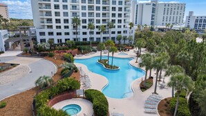 A hotel with a swimming pool, palm trees, and a view of Hilton buildings. - 4th-Floor Studio | Walk to Beach | Pool, Beach Tram | Luau II 6421, Sandestin (Miramar Beach)