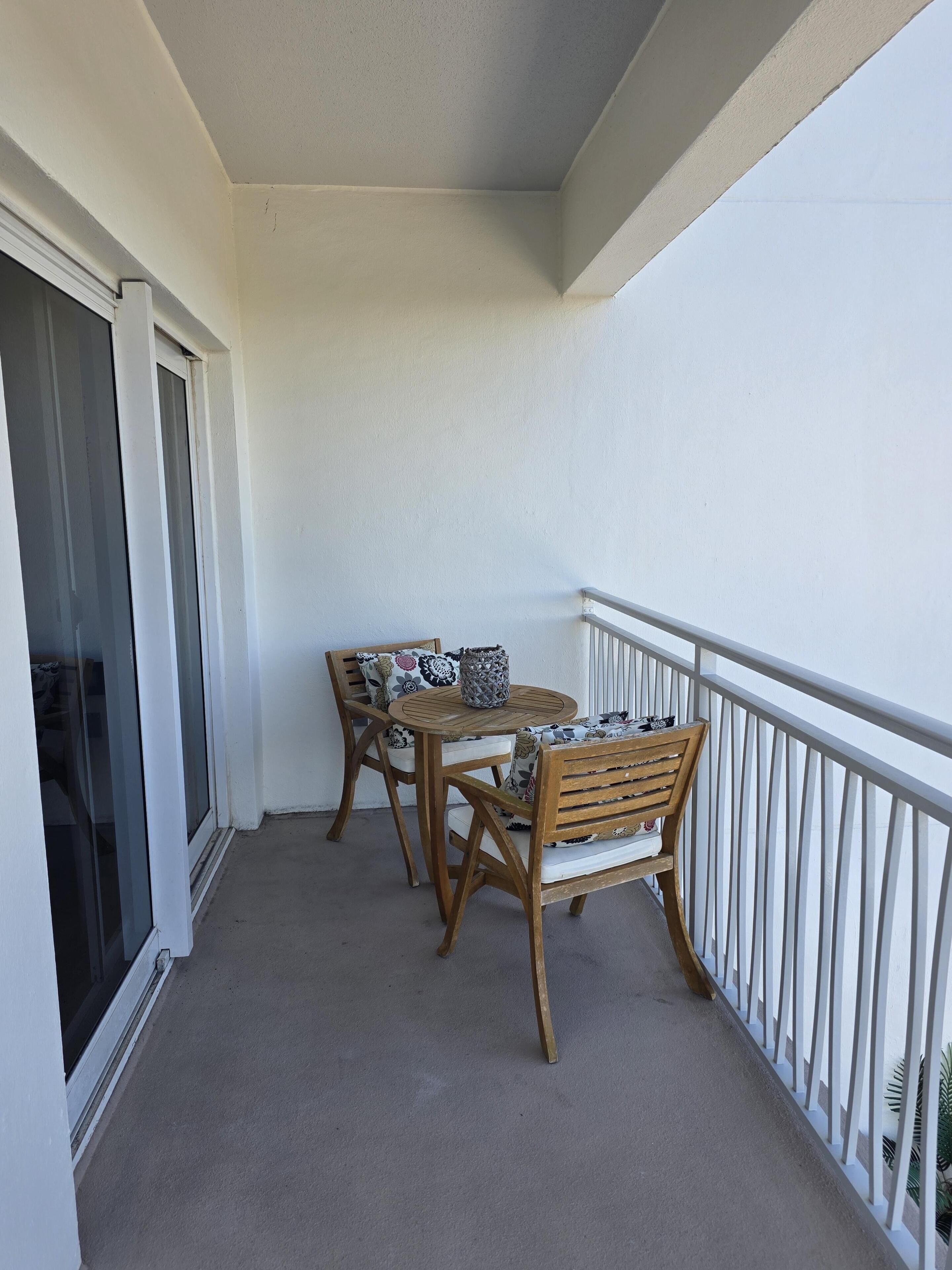 A balcony with a table and chairs, a white railing, and a sliding glass door.
