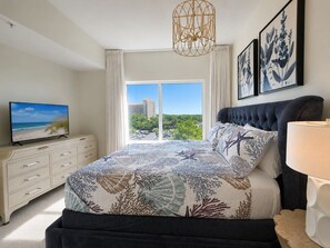 Ein Schlafzimmer mit einem Bett, einem Fernseher auf einer Kommode, einer Chandelierleuchtreihe und Kunstwerken an der Wand.