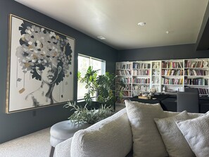 Ein modernes Wohnzimmer mit einem großen abstrakten Gemälde, einem Bücherregal, einem Sofa und einer Topfpflanze.