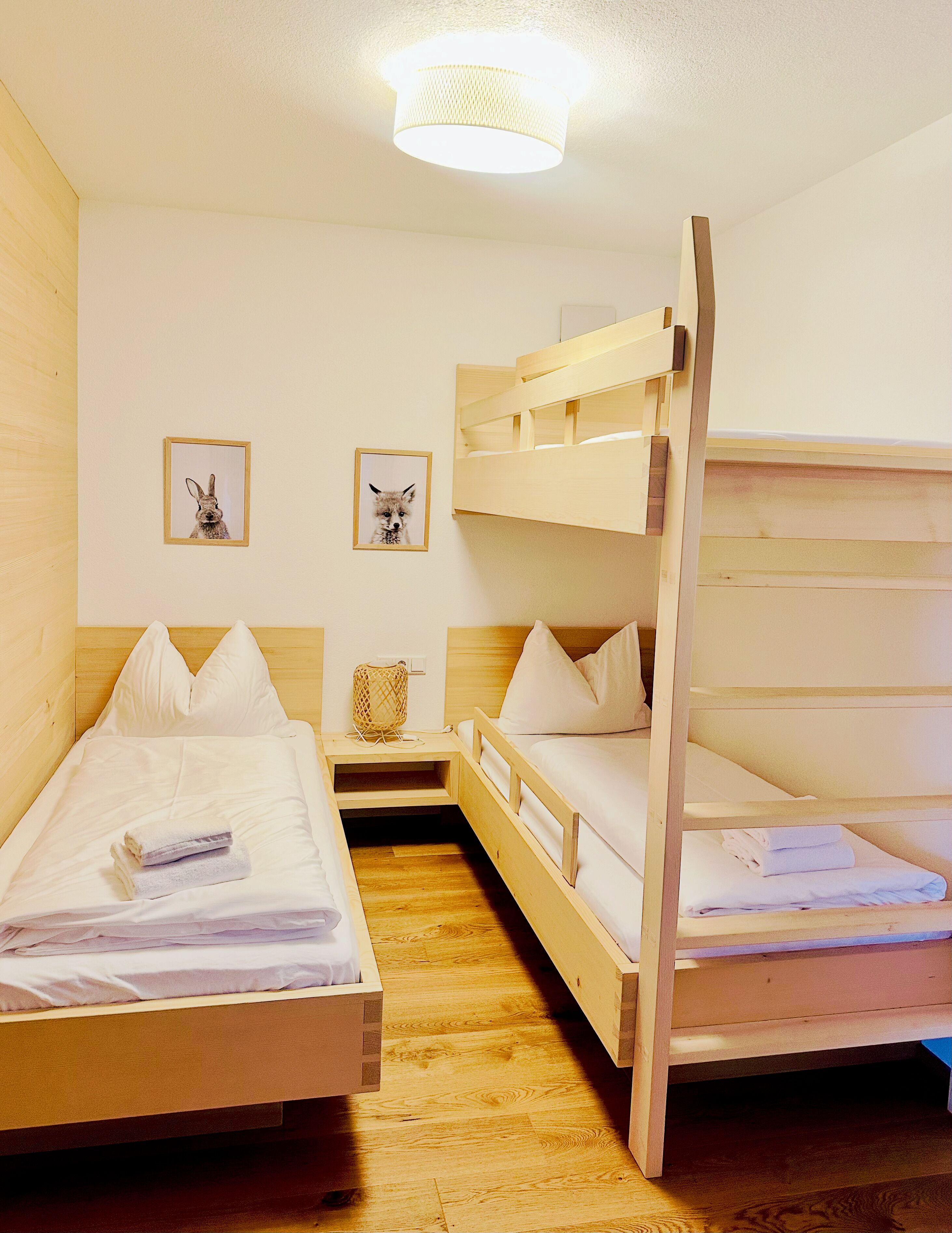 A room with two bunk beds, a bedside table with a lamp, and two framed pictures on the wall.