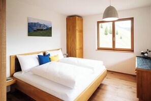 A bedroom with a bed, wooden wardrobe, a window with a view of trees, and a painting on the wall. - Landhaus Damüls (Damüls)