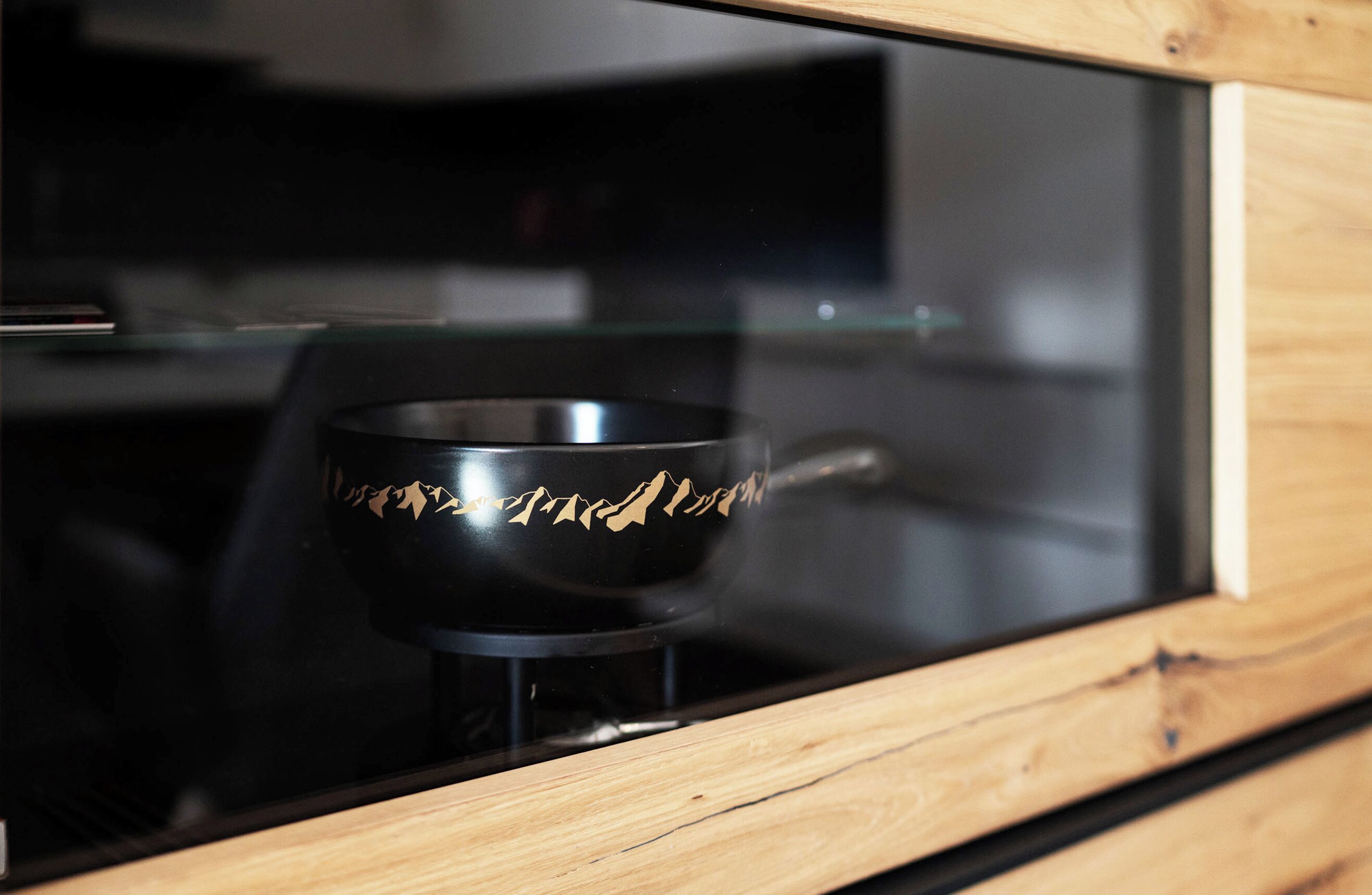 A black object with a mountain design on a stand inside a wooden-framed glass enclosure.