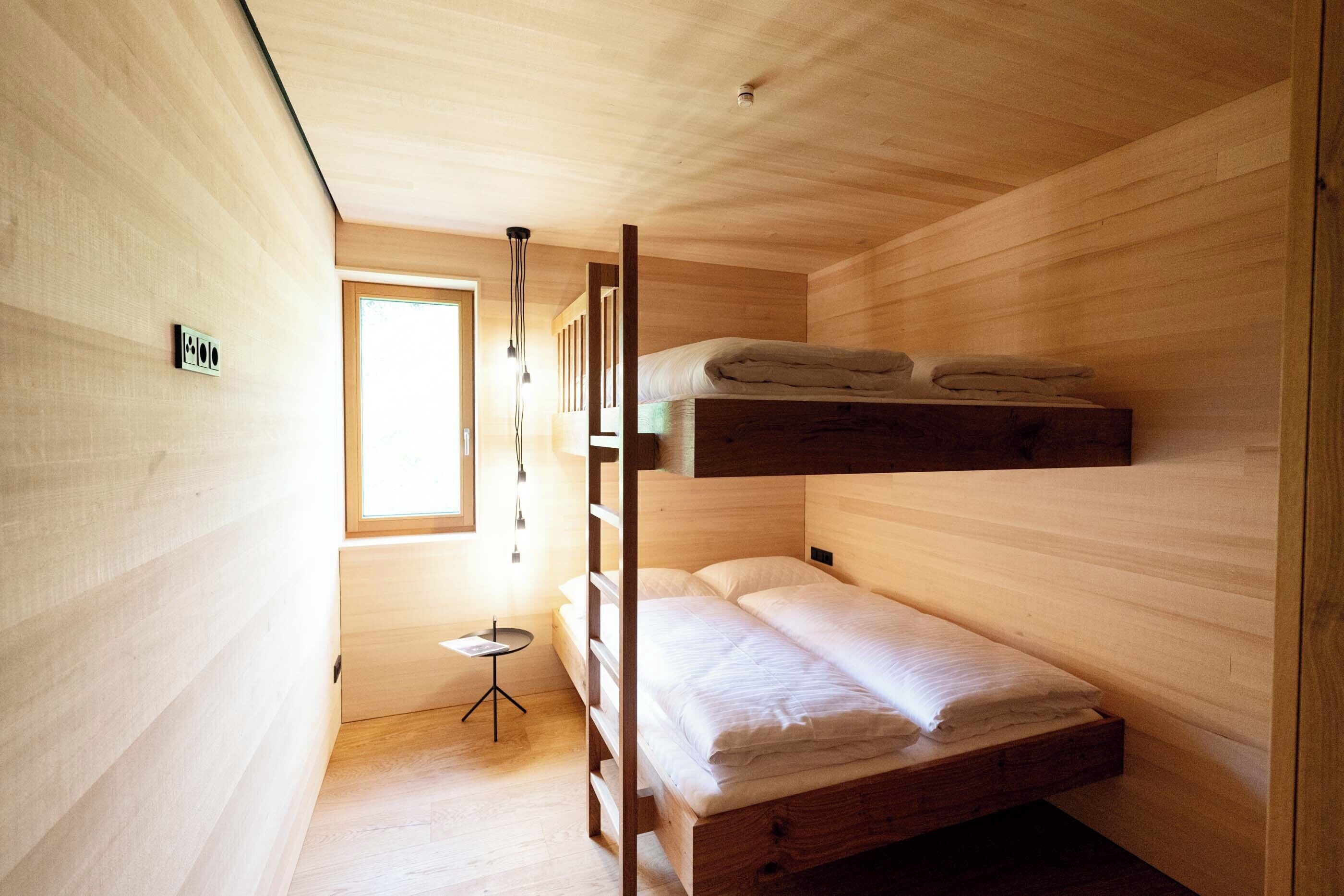 A compact wooden room with bunk beds, a small round table, and a window providing natural light.