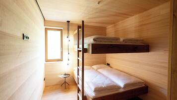 A compact wooden room with bunk beds, a small round table, and a window providing natural light.