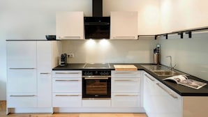 Une cuisine moderne avec des meubles blancs, une hotte noire, un four encastré et un évier en acier inoxydable.
