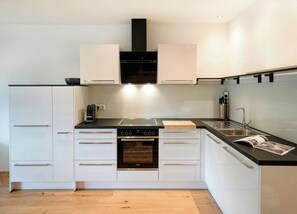 Una cocina moderna con armarios blancos, una campana extractora negra, un horno empotrado y un lavamanos de acero inoxidable.