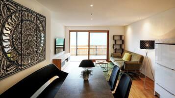 A modern living room with a dining area, a large abstract artwork on the wall, and a balcony with a wooden deck.