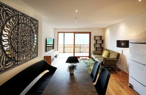 A modern living room with a dining area, a large abstract artwork on the wall, and a balcony with a wooden deck. - Landhaus Damüls (Damüls)
