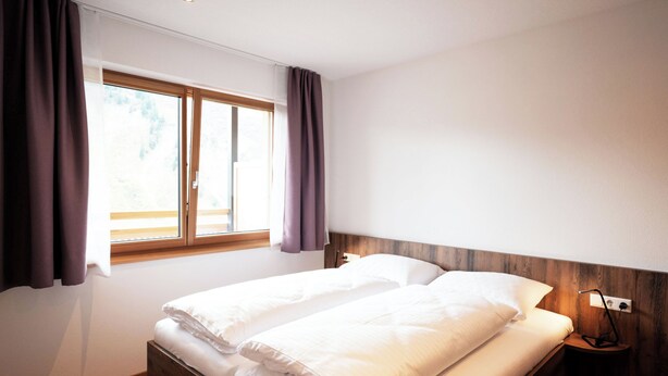 Une chambre à coucher avec un lit, une table de chevet, une fenêtre avec des rideaux et une tête de lit en bois.