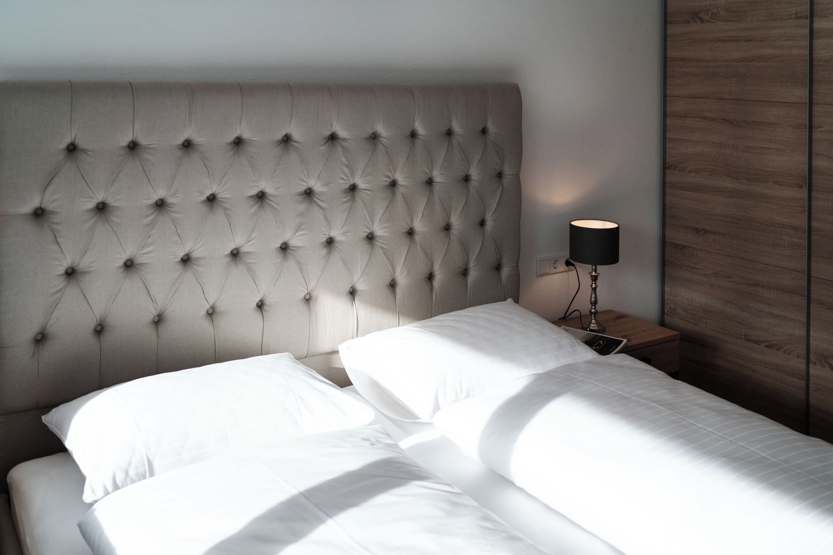 A bed with a tufted headboard, white bedding, and a bedside table with a lamp.
