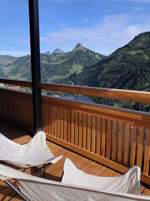 A balcony with wooden railings and white cushioned chairs, overlooking a mountainous landscape. - Landhaus Damüls (Damüls)
