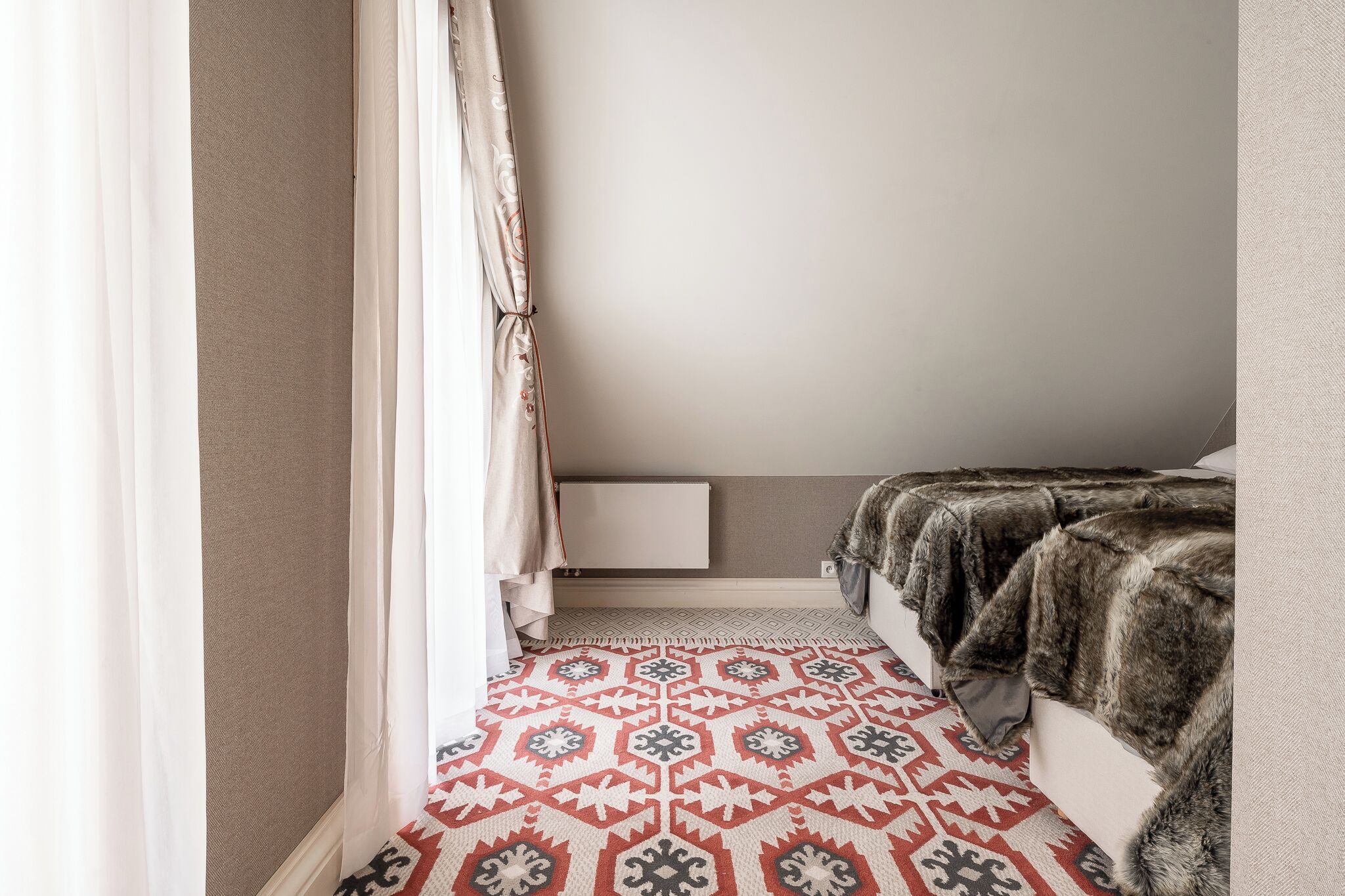 A bedroom with a patterned rug, a fur throw, and a white bedside table.
