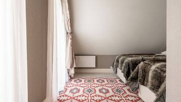 A bedroom with a patterned rug, a fur throw, and a white bedside table.
