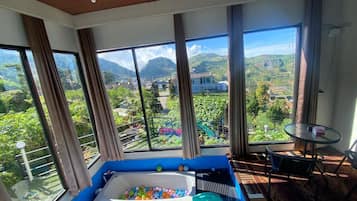 A room with large windows, a blue bathtub, a small table, and a chair.
