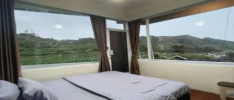 A bedroom with a bed, curtains, a window, and a view of a hilly landscape.