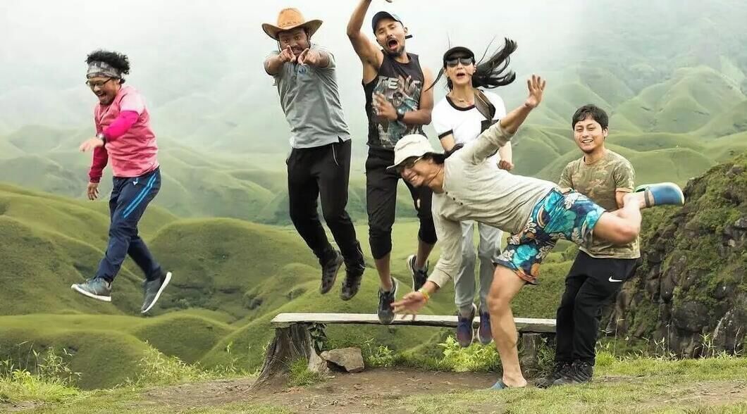 A group of people in a natural outdoor setting with a hilly landscape in the background.