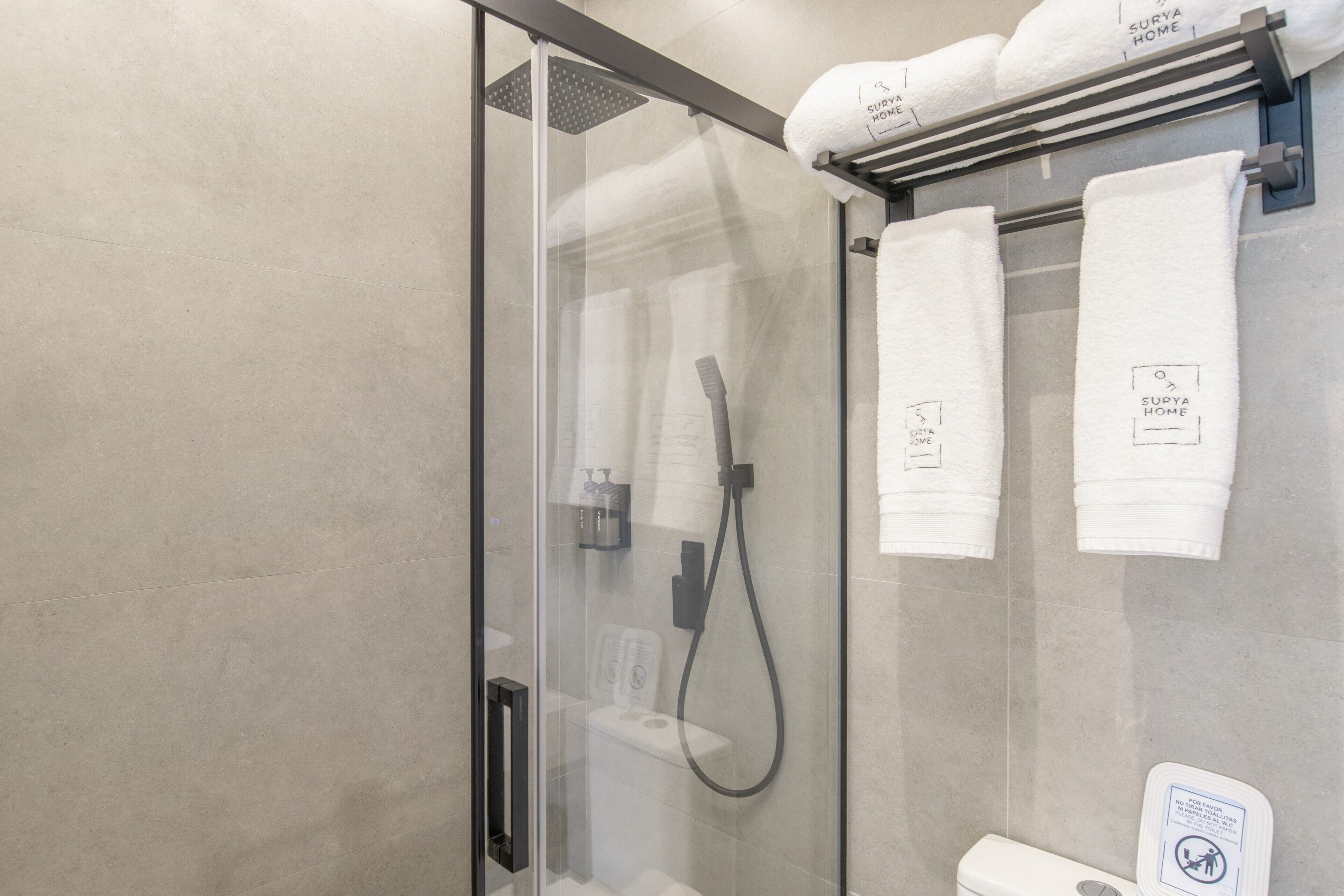 A glass-enclosed shower with a handheld showerhead, a towel rack with white towels, and a sign indicating no towel drying.