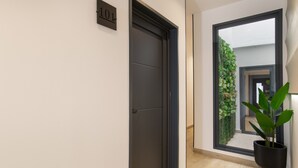 A hallway with a dark door, a number sign, a window with a view of greenery, and a potted plant. - Apartment '101' with Wi-Fi and Air Conditioning (Conil de la Frontera)