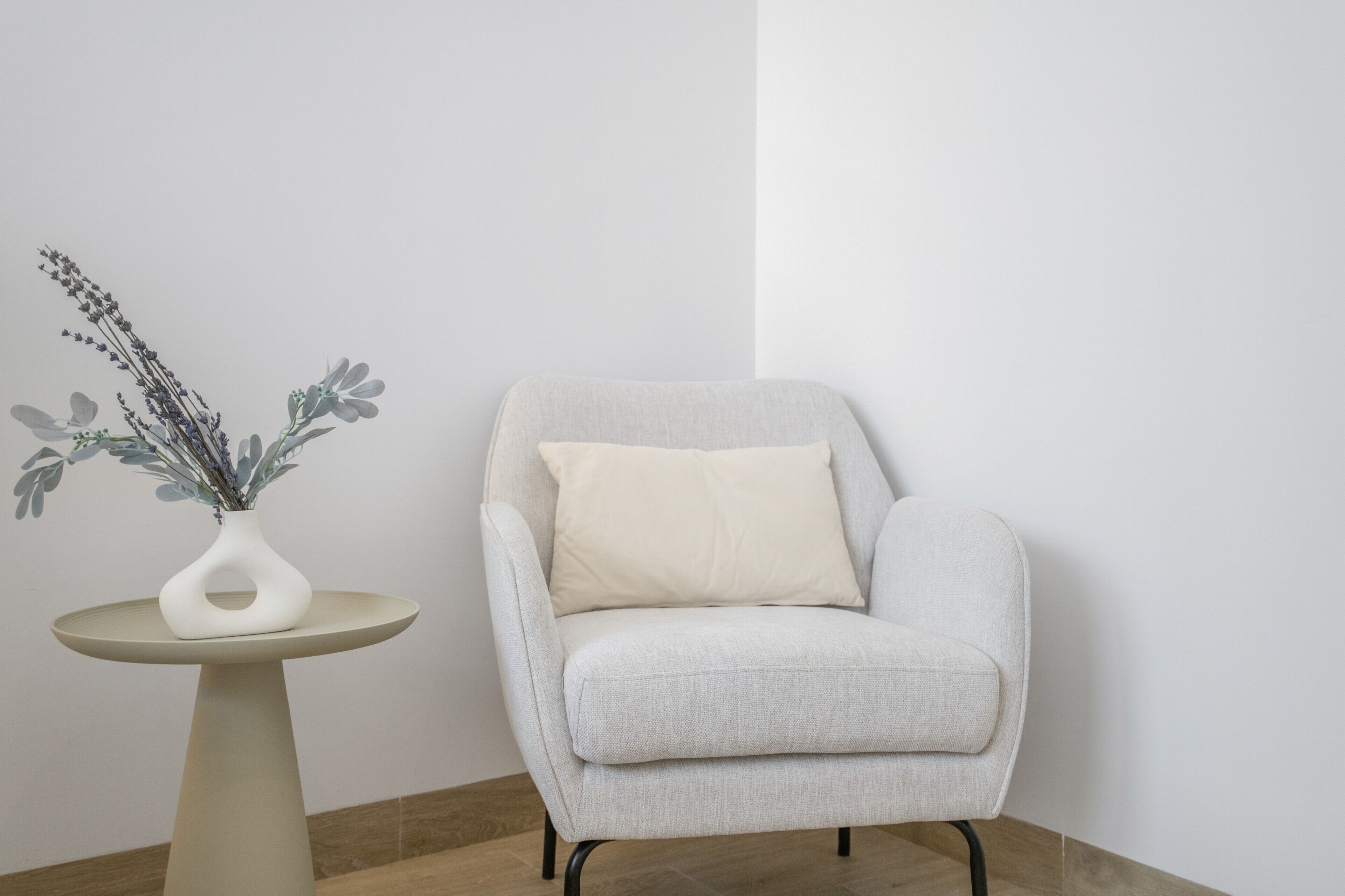 Un sillón moderno con cojín, al lado de una pequeña mesa redonda con un florero de flores secas.