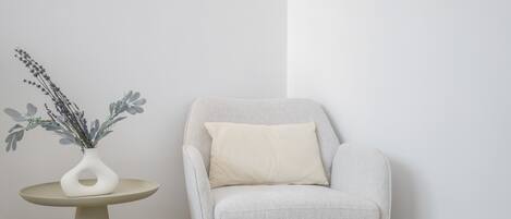 Un sillón moderno con cojín, al lado de una pequeña mesa redonda con un florero de flores secas.
