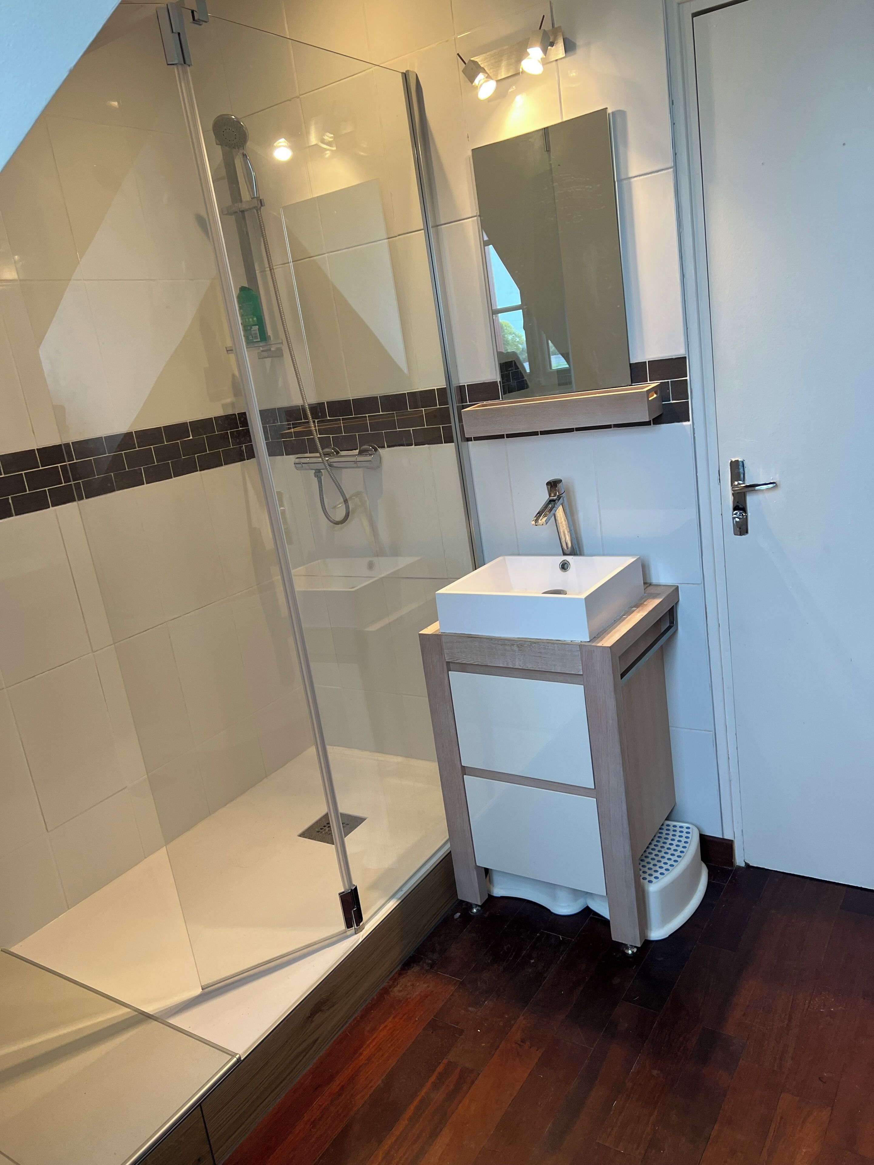 A modern bathroom with a glass shower enclosure, a white sink, and a wooden vanity.