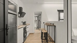 Kompakti keittiö, jossa on modernit kodinkoneet, pesukone ja pieni ruokailutila jakkaroineen.