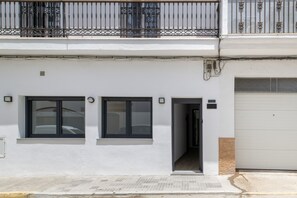 Um edifício de dois andares com fachada branca, duas janelas com molduras pretas, uma porta de garagem e uma varanda com grades de metal.
