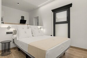 A modern hotel room with a bed, bedside table, and a small round table. - Estudio '102' con Wi-Fi y Aire Acondicionado (Conil de la Frontera)