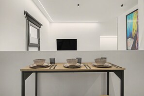Ein moderner Essbereich mit einem schlichten Tisch, gedeckt für drei Personen, mit grauen Keramikschüsseln und -tellern, einem Holztisch und einem schwarzen, an der Wand befestigten Fernseher.