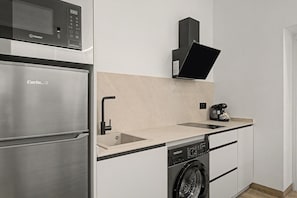Cozinha compacta com geladeira de aço inoxidável, lava-louças, cafeteira e micro-ondas.