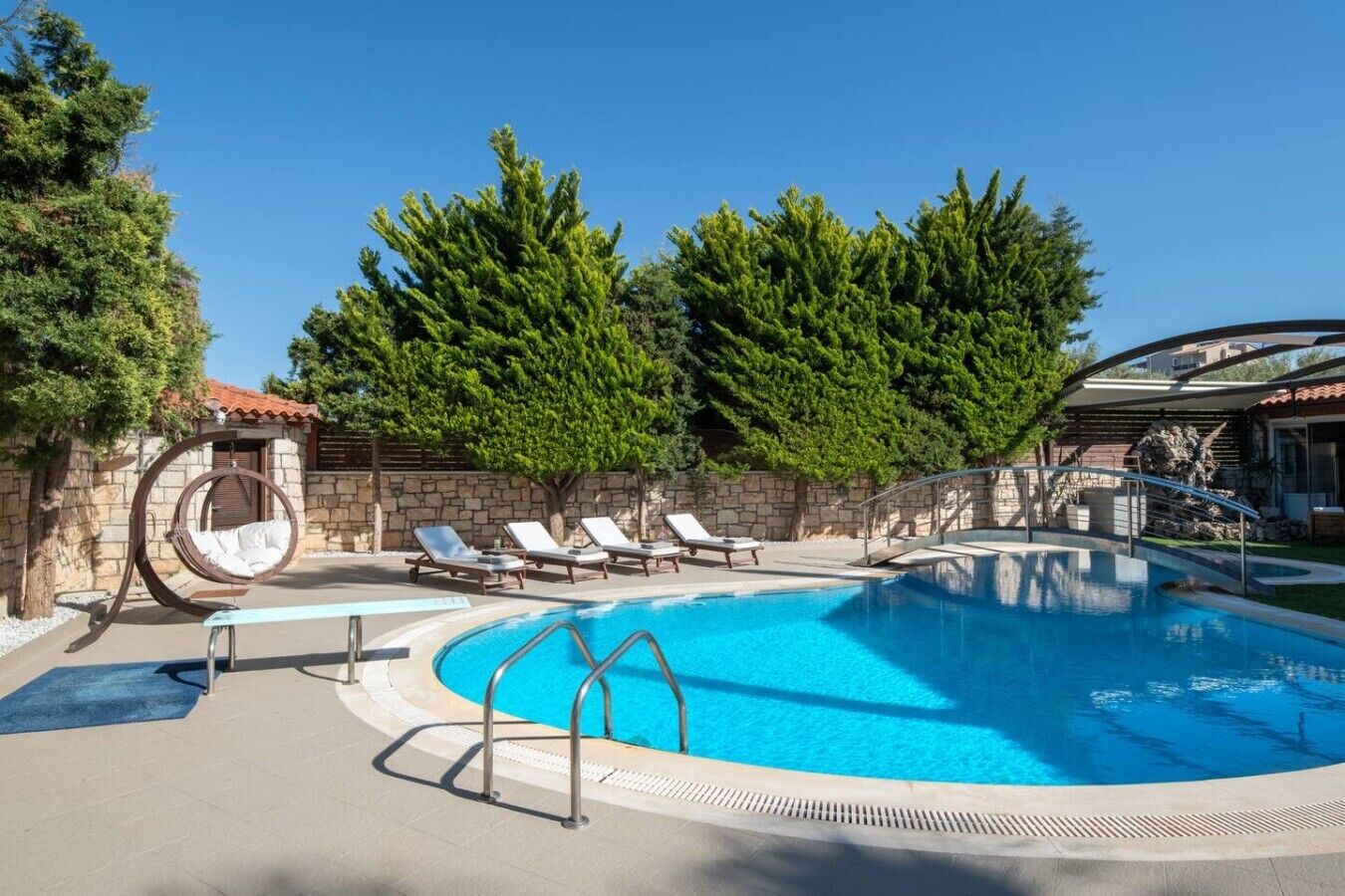 Una piscina con sillas de descanso, un muro de piedra y árboles.