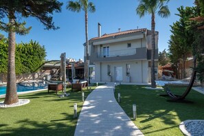 Ein modernes, zweistöckiges Haus mit Swimmingpool, Sitzgelegenheit im Freien und einem gepflegten Rasen.