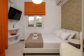 Ein Hotelzimmer mit Bett, Fernseher, Fenster mit Blick, Heizkörper und einem kleinen Regal mit Büchern.