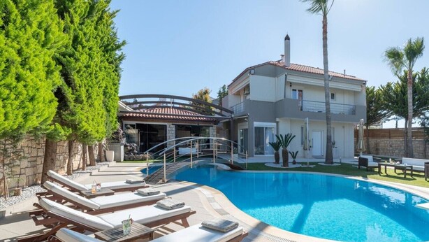 Ein modernes, zweistöckiges Haus mit Swimmingpool, Liegestühlen und einer überdachten Terrasse.