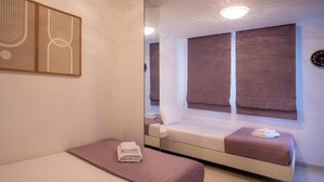 Ein Schlafzimmer mit einem Bett, einem Fenster mit Jalousien, einem Nachttisch und einem Spiegel.