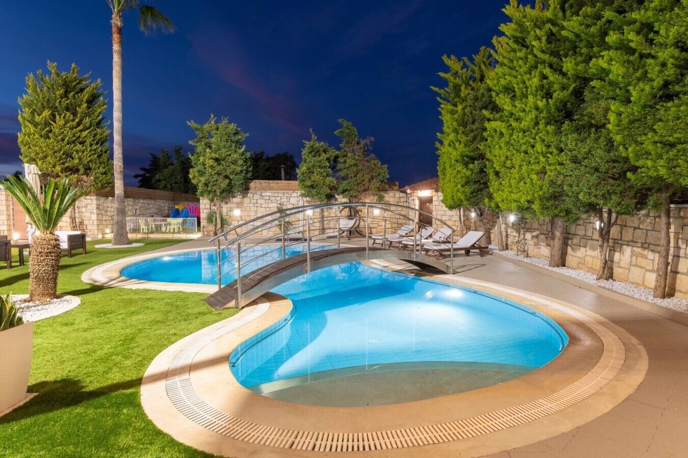 Ein Schwimmbecken mit gebogener Form, umgeben von einer Steinmauer und Bäumen.