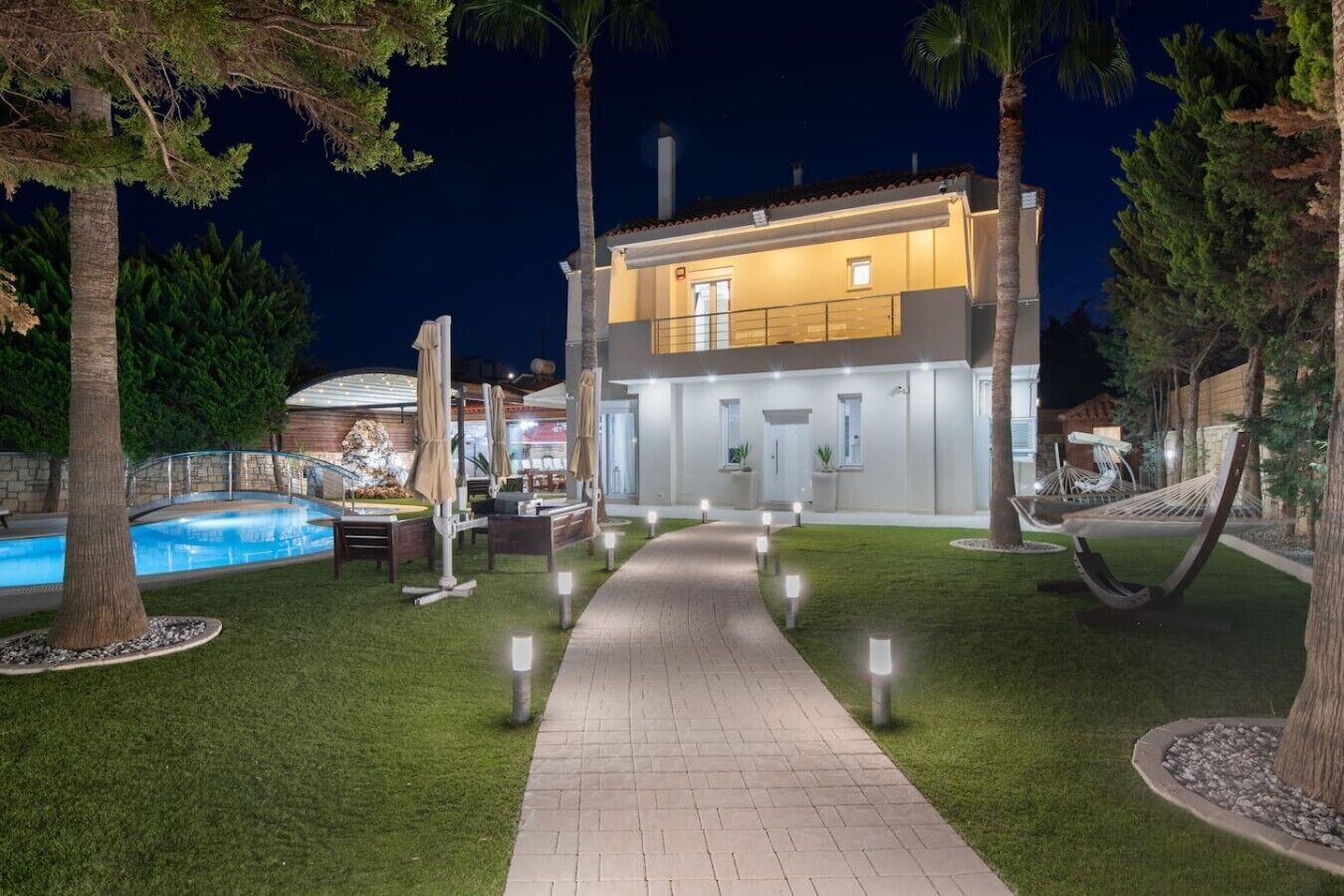 A modern two-story house with a swimming pool, outdoor seating, and a well-lit pathway.