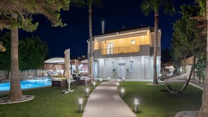 Ein modernes, zweistöckiges Haus mit Swimmingpool, Sitzgelegenheit im Freien und einem gut beleuchteten Weg.