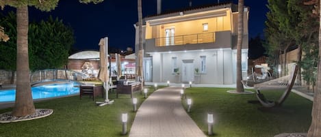 A modern two-story house with a swimming pool, outdoor seating, and a well-lit pathway.